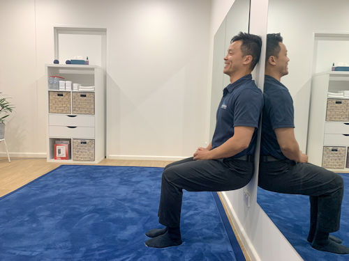 practitioner showing patient how to perform a wall sit to improve posture